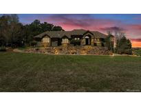 Charming exterior featuring a stone facade and manicured landscaping with a retaining wall at sunset at 19336 Queens Crescent Way, Monument, CO 80132