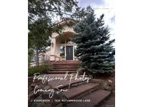Inviting front entrance with brick steps leading to a modern, light colored home with large windows and mature trees at 1425 Autumnwood Ln, Evergreen, CO 80439