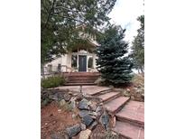 Inviting front entrance with brick steps leading to a modern, light colored home with large windows and mature trees at 1425 Autumnwood Ln, Evergreen, CO 80439