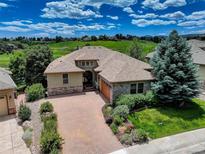 Beautiful exterior of home with stone accents, brick driveway, and lush landscaping and view of the golf course and blue sky at 11208 W Ontario Ave, Littleton, CO 80127