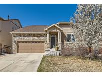 Charming stone and siding home with a well-manicured lawn and a two-car garage on a sunny day at 5181 Delphinium Cir, Brighton, CO 80601