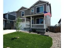 Charming two-story home featuring a covered front porch and a well-manicured lawn with an American flag at 2300 Mountain Sky Dr, Fort Lupton, CO 80621