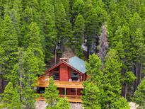 A cozy cabin nestled among tall trees boasts a large deck and rustic charm, perfect for mountain living at 489 Harris Dr, Idaho Springs, CO 80452