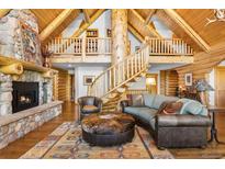 Grand living room with stone fireplace, a tree-trunk column, and log-cabin walls exudes rustic elegance at 6150 Bluebell Ln, Evergreen, CO 80439
