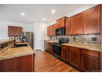 Well-lit kitchen features wood cabinets, stainless steel appliances, tile backsplash and wood flooring at 1788 Taos St, Brighton, CO 80603