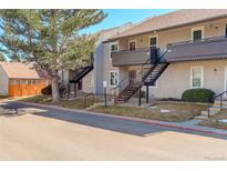 A charming exterior view of a two-story home with a beautiful tree and black metal staircases leading to the units at 7165 S Gaylord St # E09, Centennial, CO 80122