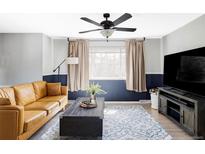 A modern living room features a stylish ceiling fan, a brown leather couch, and a blue patterned rug at 13055 E Dakota Ave, Aurora, CO 80012