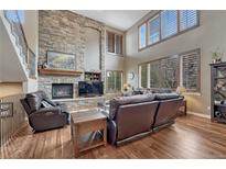 Cozy living room with a stone fireplace, hardwood floors, and plentiful windows to allow lots of natural light at 8707 Windhaven Dr, Parker, CO 80134