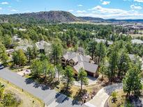 Stunning aerial view of a home nestled among trees with mountain backdrop and adjacent golf course at 648 Ruby Trust Dr, Castle Rock, CO 80108