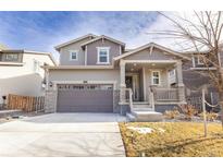 Charming two-story home features a covered porch, gray siding, stone accents, and attached two car garage at 10962 Vaughn St, Commerce City, CO 80022