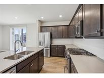 Modern kitchen boasts stainless appliances, dark wood cabinets, and a spacious island with a sink at 21185 E 62Nd Ave, Aurora, CO 80019