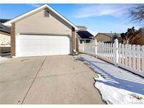 Inviting home featuring a two-car garage, brick accents, and a charming white picket fence at 14423 E 47Th Ave, Denver, CO 80239