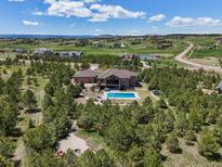 A beautiful home with an in-ground pool is surrounded by trees and green landscape in an aerial shot at 1505 Castlecombe Ln, Monument, CO 80132