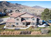 Stunning two-story home with a stone and stucco exterior, lush landscaping, and a tile roof against a mountain backdrop at 16226 River Haven Way, Morrison, CO 80465