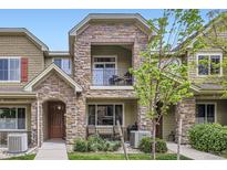 Two-story townhome featuring stone accents, second story balcony, and manicured front lawn at 15362 W 66Th Ave # D, Arvada, CO 80007