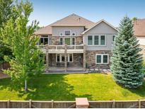 A two-story home showcasing a lush backyard, a stone patio, and a charming balcony on the second story at 13943 W 87Th Ln, Arvada, CO 80005