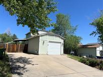 View of the home's garage with a large driveway and mature landscaping at 17477 E Temple Dr, Aurora, CO 80015