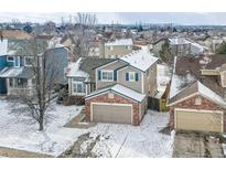Two-story home featuring a brick front, gray siding, blue shutters, and a two-car garage, all dusted with snow at 10973 Cannonade Dr, Parker, CO 80138