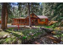 Charming cabin with a creek, bridge, and a spacious wrap-around porch surrounded by lush greenery at 27802 Shadow Mountain Dr, Conifer, CO 80433