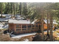 Inviting log cabin with a covered porch nestled among tall pine trees and snow at 27802 Shadow Mountain Dr, Conifer, CO 80433