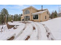 Charming home exterior with large windows and snowy landscape, set against a backdrop of evergreen trees at 27987 Pine Grove Trl, Conifer, CO 80433