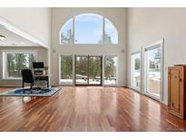 Bright living room with hardwood floors, large arched window, and sliding glass doors at 27987 Pine Grove Trl, Conifer, CO 80433
