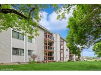Condo building with a large lawn and several balconies is partially framed by mature trees at 8654 Decatur St # 251, Westminster, CO 80031