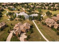 Stunning aerial view of a home with mature landscaping and a community pond at 5069 Castle Pines S Dr, Castle Rock, CO 80108