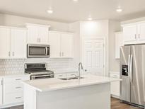 Bright kitchen features white cabinets, stainless steel appliances, and a stylish tile backsplash at 17417 E 89Th Way, Commerce City, CO 80022