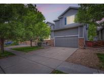 Charming two-story home with gray siding, stone accents, mature trees, and a two car garage at 12125 Helena St, Brighton, CO 80603