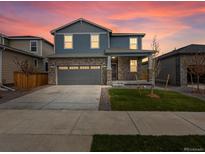 Charming two-story home with stone accents, a two-car garage, a well-maintained lawn and colorful sunset at 546 Red Rock Pl, Brighton, CO 80601