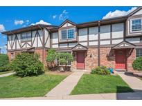 Charming townhome featuring brick facade, Tudor-style accents, manicured lawn, and inviting red front door at 3855 S Monaco St # 182, Denver, CO 80237