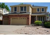 Two-story tan and brick home with a three-car garage, well-manicured lawn, and a cozy covered front porch at 20630 E Hamilton Ave, Aurora, CO 80013