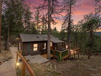 Charming cabin nestled among the trees, featuring a wooden deck and quaint exterior lighting at 4786 Forest Hill Rd, Evergreen, CO 80439