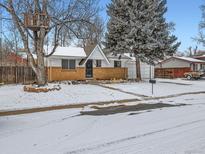 Charming single-story home with a brick facade, snow-covered yard, mature tree, and a whimsical treehouse at 469 S Routt Way, Lakewood, CO 80226
