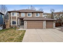 Traditional two-story home featuring a three-car garage, brown siding, and manicured lawn at 6427 S Urban Ct, Littleton, CO 80127