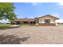 Ranch-style home featuring a brick facade, covered porch and a gravel driveway under a blue sky at 1851 E 138Th Ave, Brighton, CO 80602