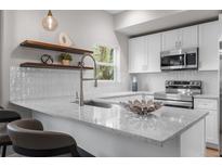 Modern kitchen featuring white cabinets, stainless steel appliances, quartz countertops, and stylish floating shelves at 2140 S Ash St # 102, Denver, CO 80222