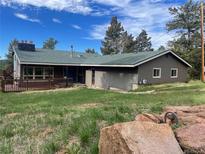 Charming single-story home with brown siding, green roof, deck, and a large boulder in the foreground at 11608 Apache Trl, Conifer, CO 80433