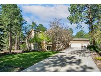 Tan two-story home with mature trees and a long driveway leading to a three-car garage at 20190 Deer Shadow Way, Monument, CO 80132
