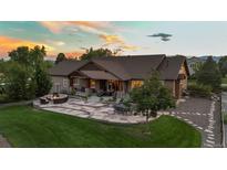 Expansive backyard features stone patio with a built-in fire pit and seating, manicured lawn, and the house at sunset at 7130 Independence St, Arvada, CO 80004
