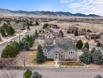 Stunning gray two-story home featuring a white fence, lush lawn, mature trees, and picturesque mountain views at 5753 Secrest Ct, Golden, CO 80403