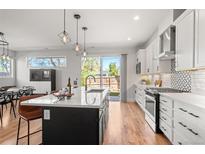 Bright kitchen features a center island, modern lighting, white cabinetry, stainless appliances, and backyard access at 5240 N Raleigh St, Denver, CO 80212