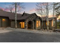 Charming home exterior featuring a stone archway entrance, mature trees, and manicured landscaping at 58 Stagecoach Blvd, Evergreen, CO 80439