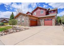 Inviting two-story home featuring stone accents, red siding, a spacious driveway and attached two-car garage at 7999 S Blackstone Pkwy, Aurora, CO 80016