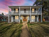 Charming two-story home featuring a double balcony, white facade, and welcoming front yard at 1100 Hudson St, Denver, CO 80220