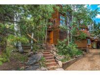 Charming cabin-style home with wood siding and inviting stone staircase surrounded by lush trees at 1575 York Gulch Rd, Idaho Springs, CO 80452