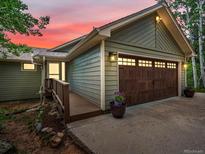 Charming home featuring a brown garage door, wood-paneled siding, and a sunset background at 30382 Kings Valley East, Conifer, CO 80433