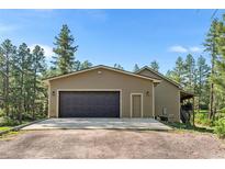Attached two-car garage with dark wood doors and durable concrete driveway surrounded by natural landscape at 11044 Conestoga Pl, Franktown, CO 80116