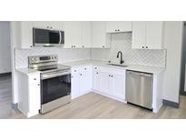 Modern kitchen with white cabinets, stainless steel appliances, and herringbone backsplash at 7810 Larkwood St, Commerce City, CO 80022